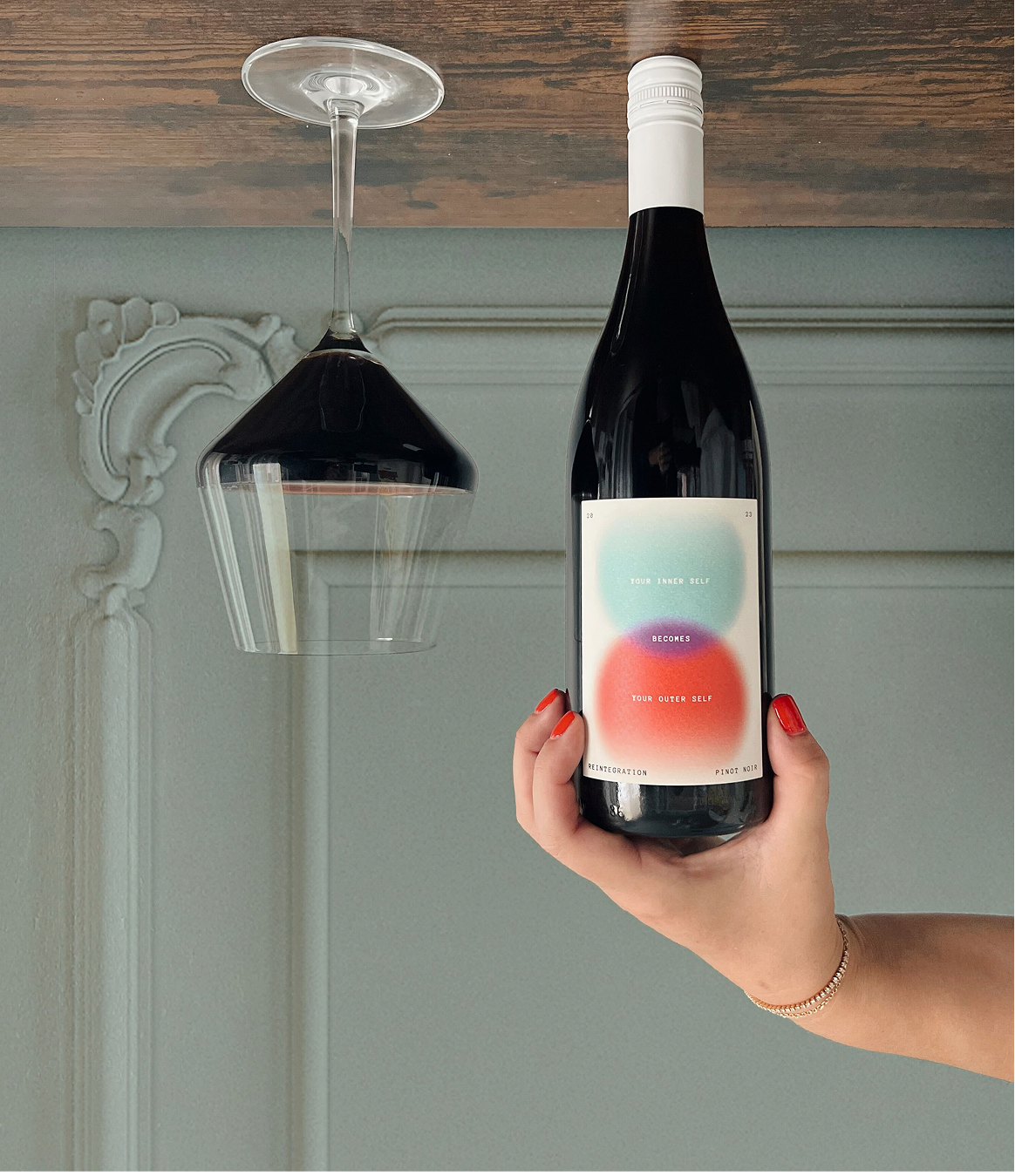 Person holding a wine bottle with a colorful label against a neutral background